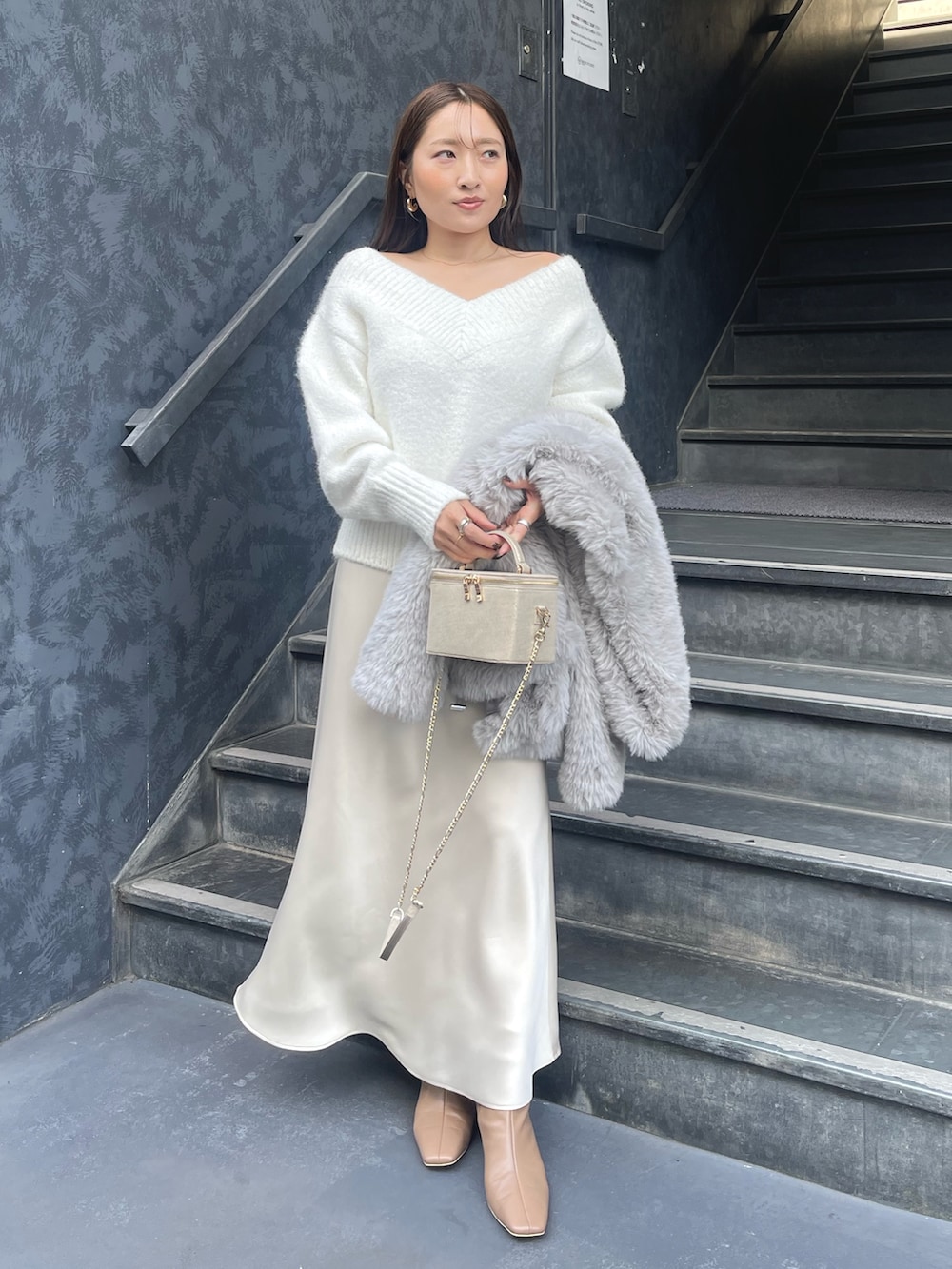 ホワイト系のニット/セーター、グレー系のその他アウター、ゴールド系のハンドバッグを着用したレディースの冬コーディネートの2枚目の写真