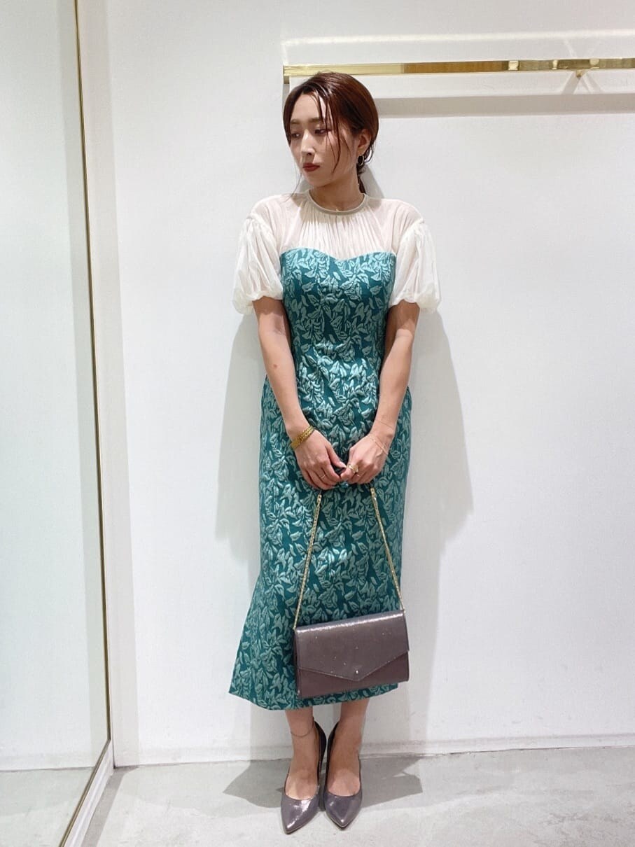 シルバー系のクラッチバッグ、シルバー系のパンプス、グリーン系のドレスを着用したレディースの秋コーディネートの2枚目の写真
