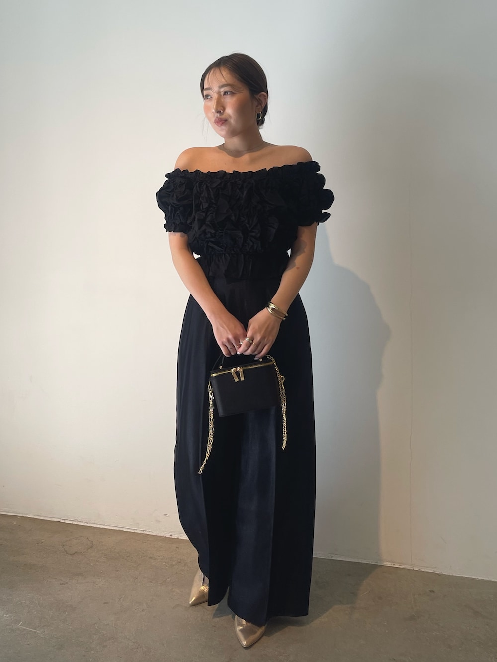 ブラック系のハンドバッグ、ゴールド系のパンプス、ブラック系のパンツドレスを着用したレディースの春コーディネートの2枚目の写真