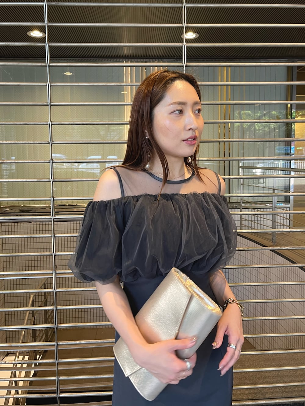 グレー系のドレス、ゴールド系のクラッチバッグ、ゴールド系のピアス（両耳用）を着用したレディースの夏コーディネートの10枚目の写真