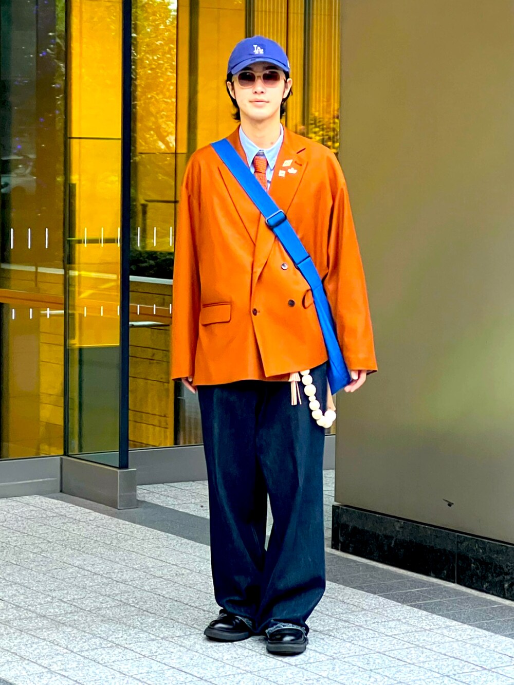 ブルー系のデニムパンツ、ブラック系のブーツ、オレンジ系のバッグを着用したメンズの秋コーディネートの3枚目の写真