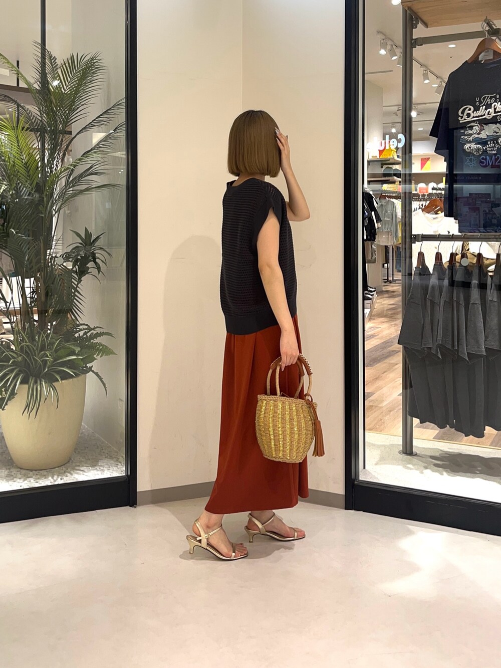 グレー系のニット/セーター、ベージュ系のバッグ、オレンジ系のワンピースを着用したレディースの夏コーディネートの3枚目の写真