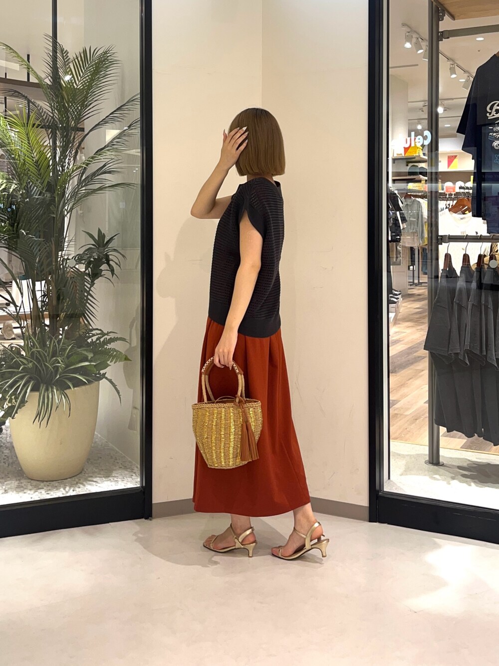 グレー系のニット/セーター、ベージュ系のバッグ、オレンジ系のワンピースを着用したレディースの夏コーディネートの2枚目の写真