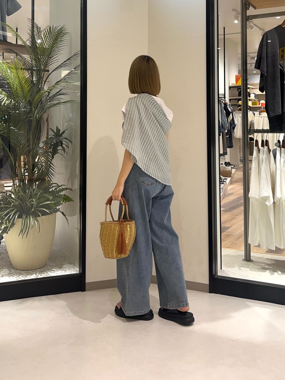 ベージュ系のバッグ、ブルー系のデニムパンツ、ブラック系のシューズを着用したレディースの夏コーディネートの2枚目の写真