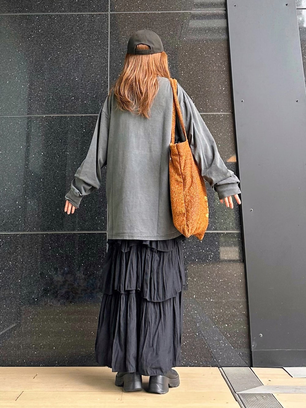 ブラック系のTシャツ/カットソー、ブラック系のスカート、オレンジ系のトートバッグを着用したレディースの秋コーディネートの4枚目の写真