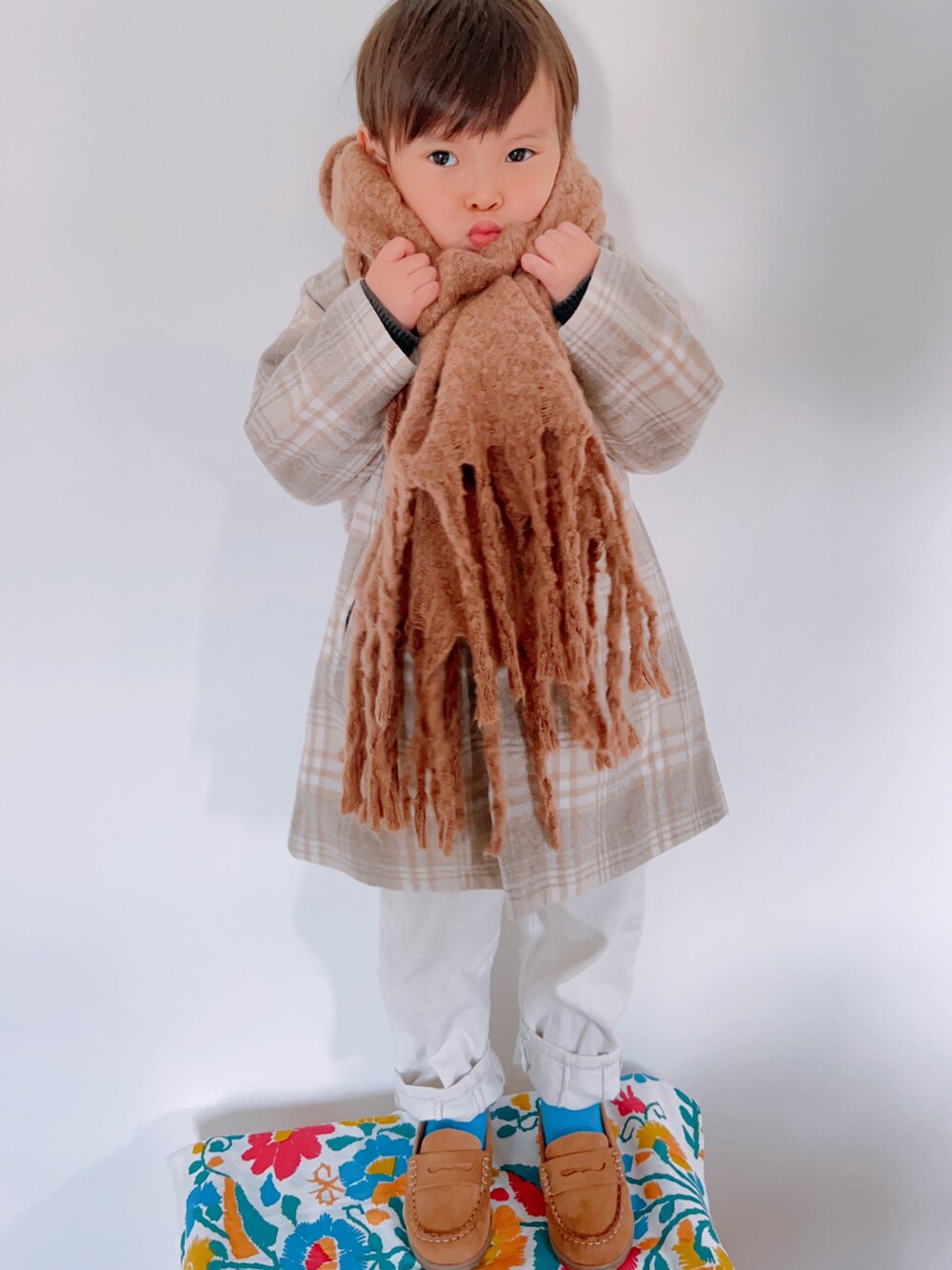 ベージュ系のチェスターコート、グレー系のニット/セーター、ホワイト系のパンツを着用したキッズの秋コーディネートの5枚目の写真