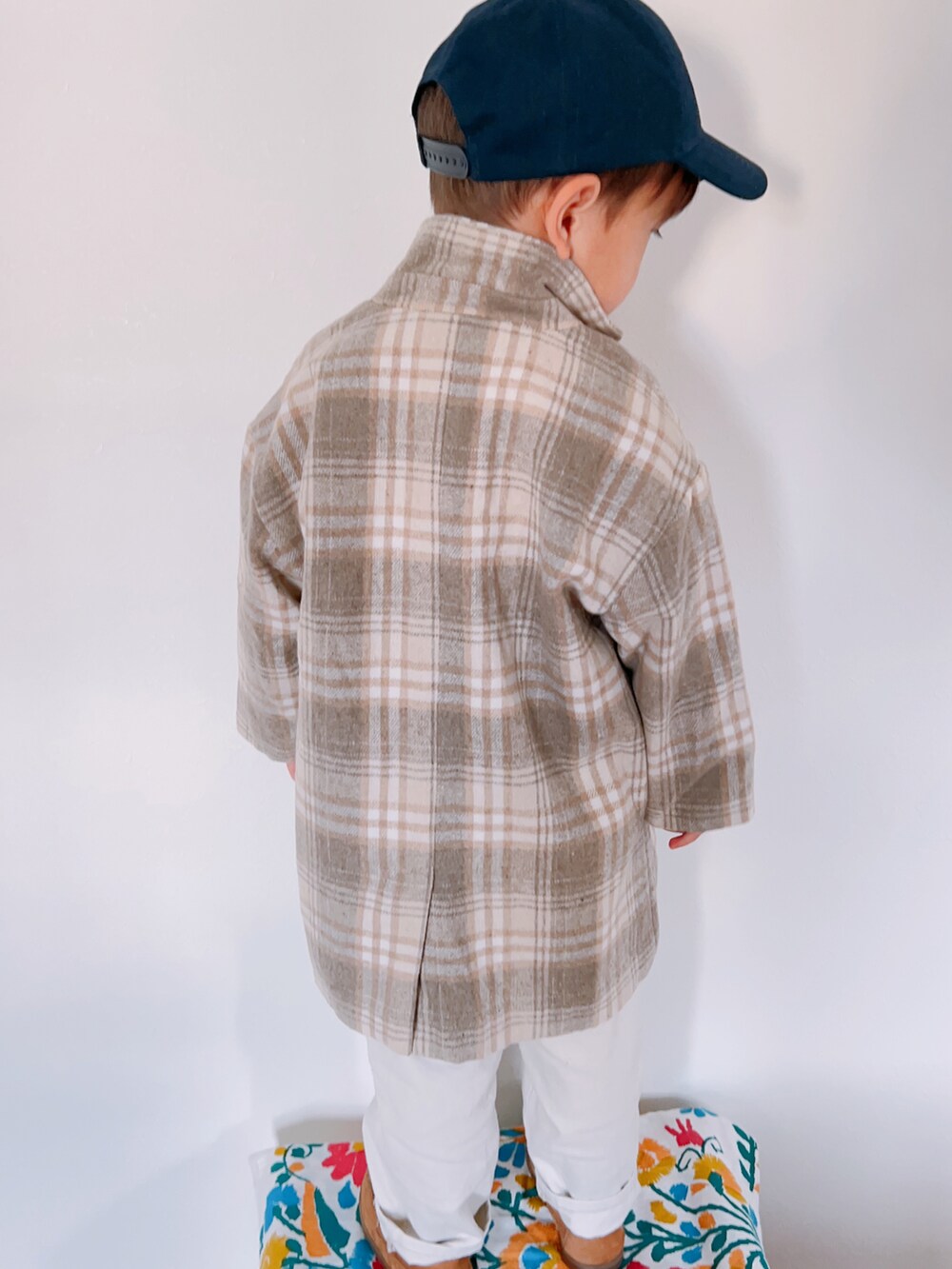 ベージュ系のチェスターコート、グレー系のニット/セーター、ホワイト系のパンツを着用したキッズの秋コーディネートの3枚目の写真