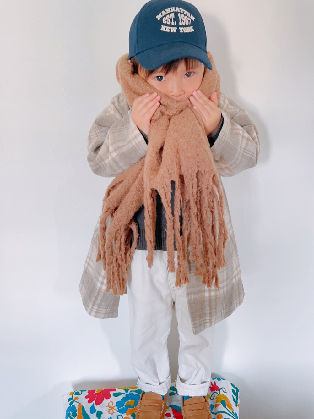 ベージュ系のチェスターコート、グレー系のニット/セーター、ホワイト系のパンツを着用したキッズの秋コーディネートの2枚目の写真