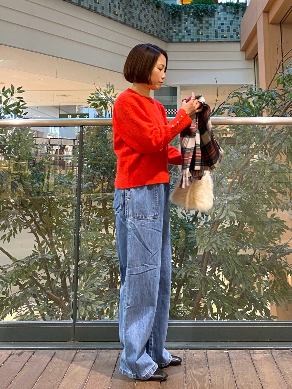 レッド系のニット/セーター、ブルー系のデニムパンツ、ベージュ系のハンドバッグを着用したレディースの冬コーディネートの3枚目の写真