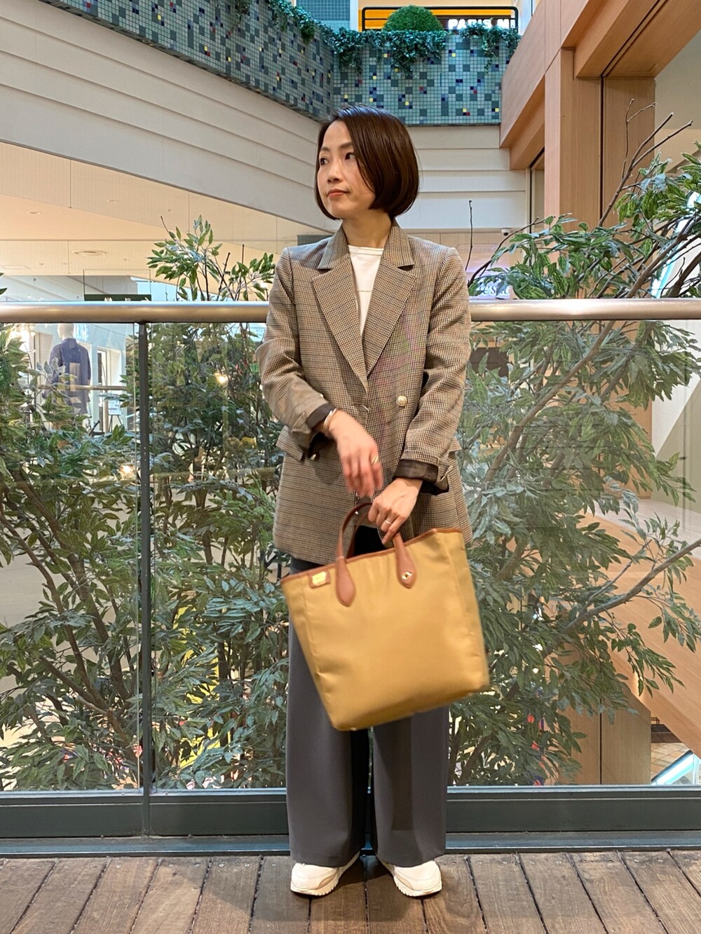 ベージュ系のテーラードジャケット、ホワイト系のベスト、イエロー系のショルダーバッグを着用したレディースの秋コーディネートの2枚目の写真