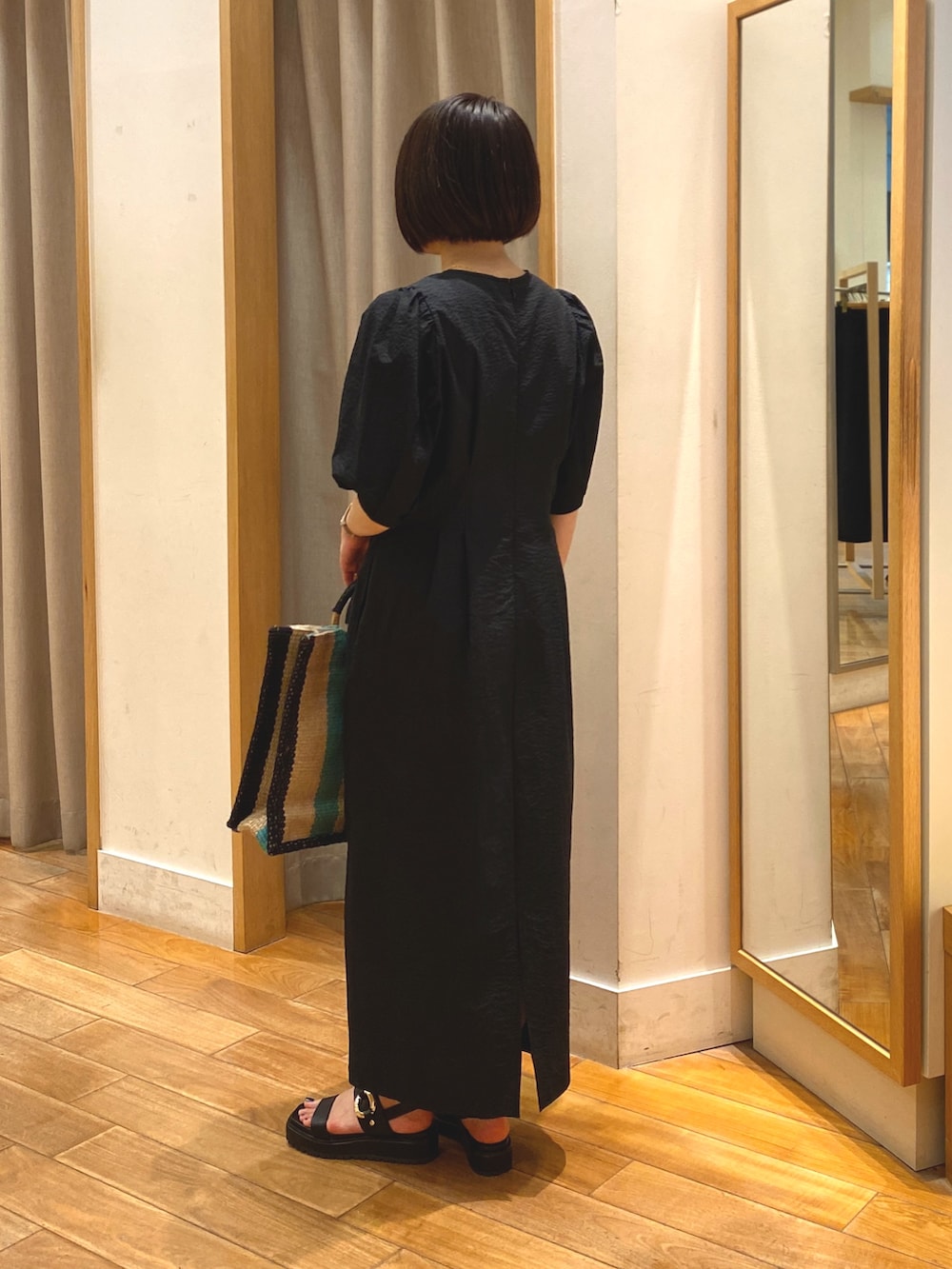 ブラック系のワンピース、ベージュ系のかごバッグ、ゴールド系のネックレスを着用したレディースの春コーディネートの6枚目の写真