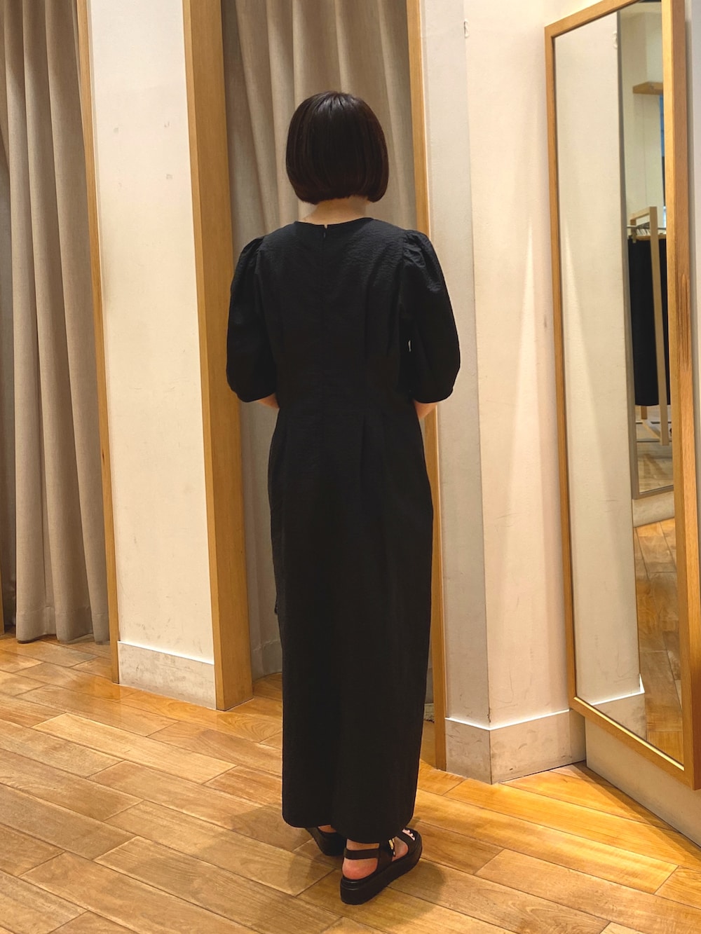 ブラック系のワンピース、ベージュ系のかごバッグ、ゴールド系のネックレスを着用したレディースの春コーディネートの7枚目の写真