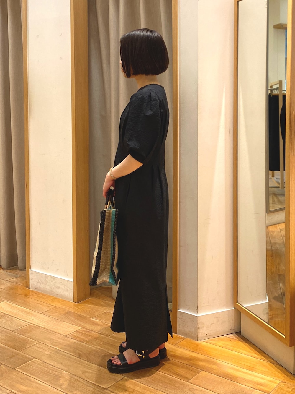 ブラック系のワンピース、ベージュ系のかごバッグ、ゴールド系のネックレスを着用したレディースの春コーディネートの4枚目の写真