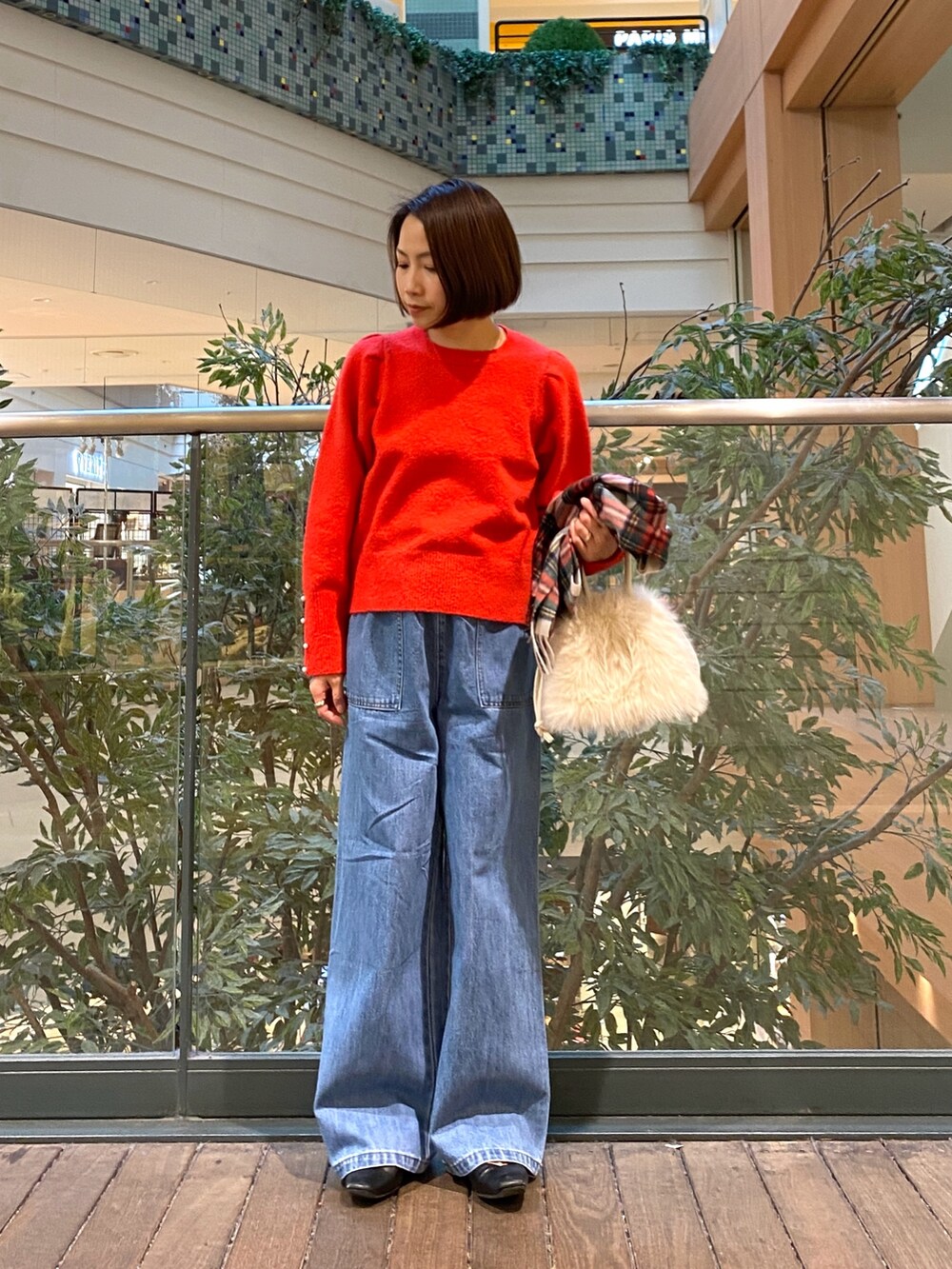 レッド系のニット/セーター、ブルー系のデニムパンツ、ベージュ系のハンドバッグを着用したレディースの冬コーディネートの2枚目の写真