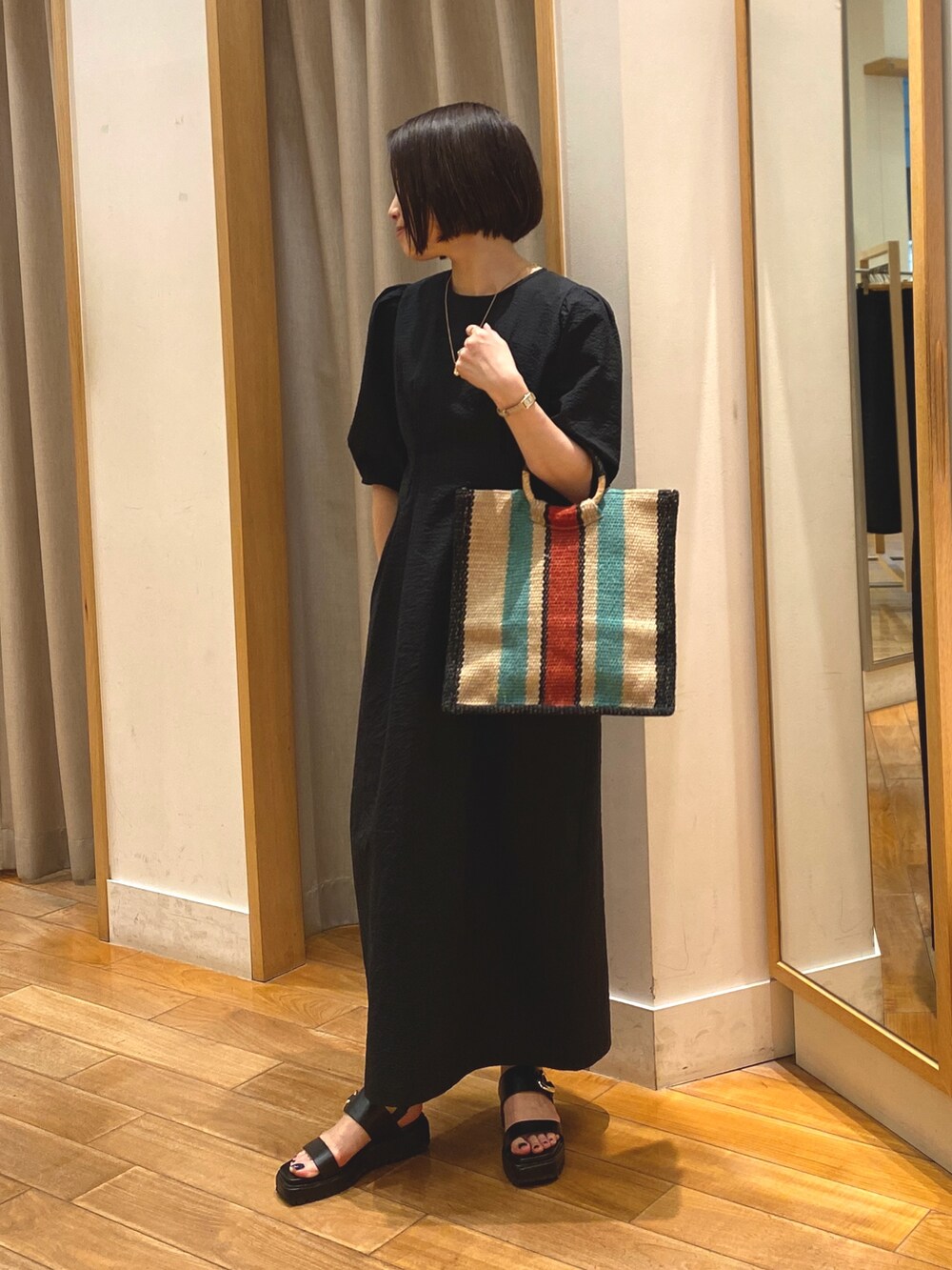 ブラック系のワンピース、ベージュ系のかごバッグ、ゴールド系のネックレスを着用したレディースの春コーディネートの2枚目の写真