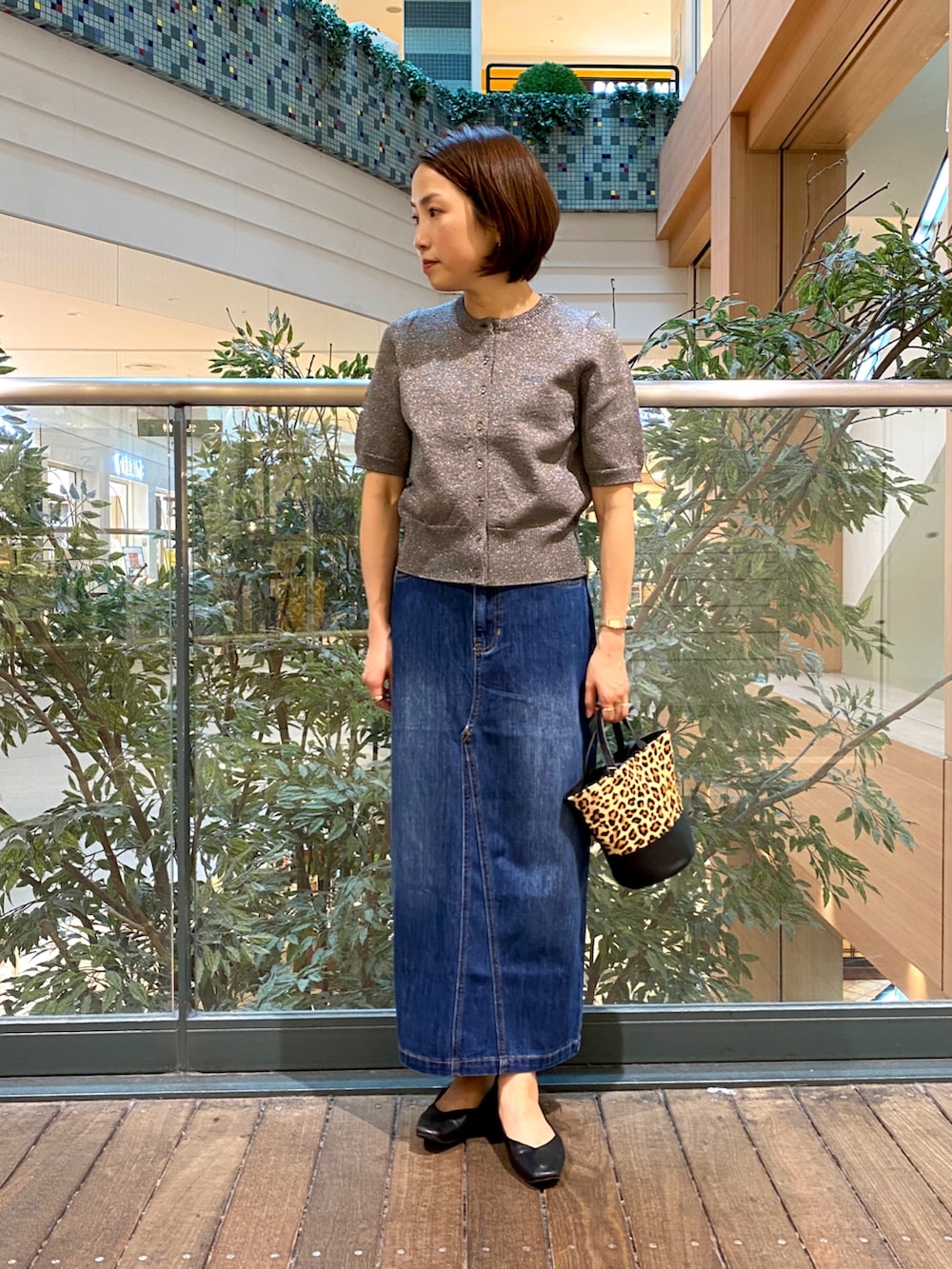 グレー系のニット/セーター、ブルー系のデニムスカート、ベージュ系のショルダーバッグを着用したレディースの秋コーディネートの2枚目の写真