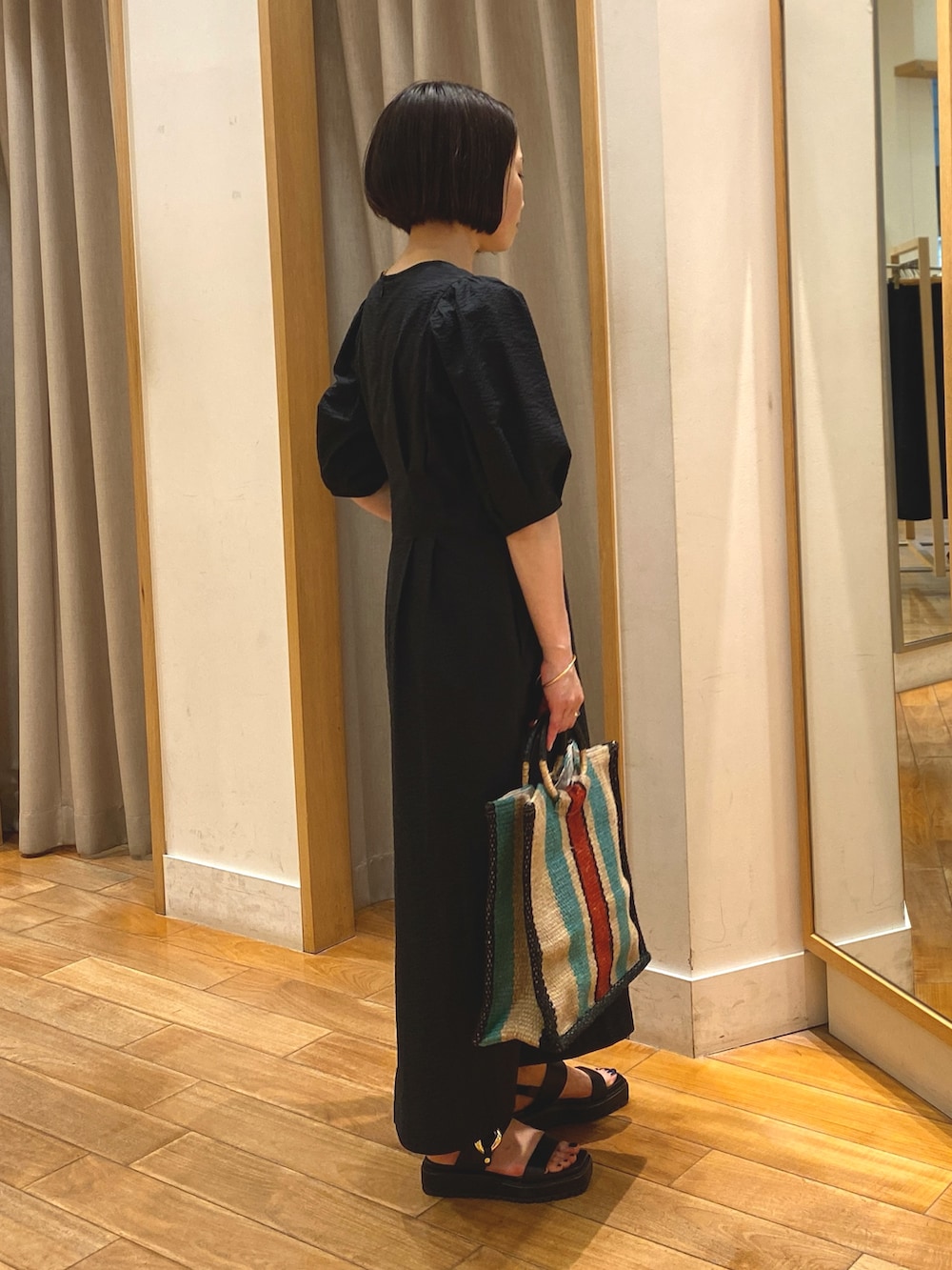 ブラック系のワンピース、ベージュ系のかごバッグ、ゴールド系のネックレスを着用したレディースの春コーディネートの5枚目の写真