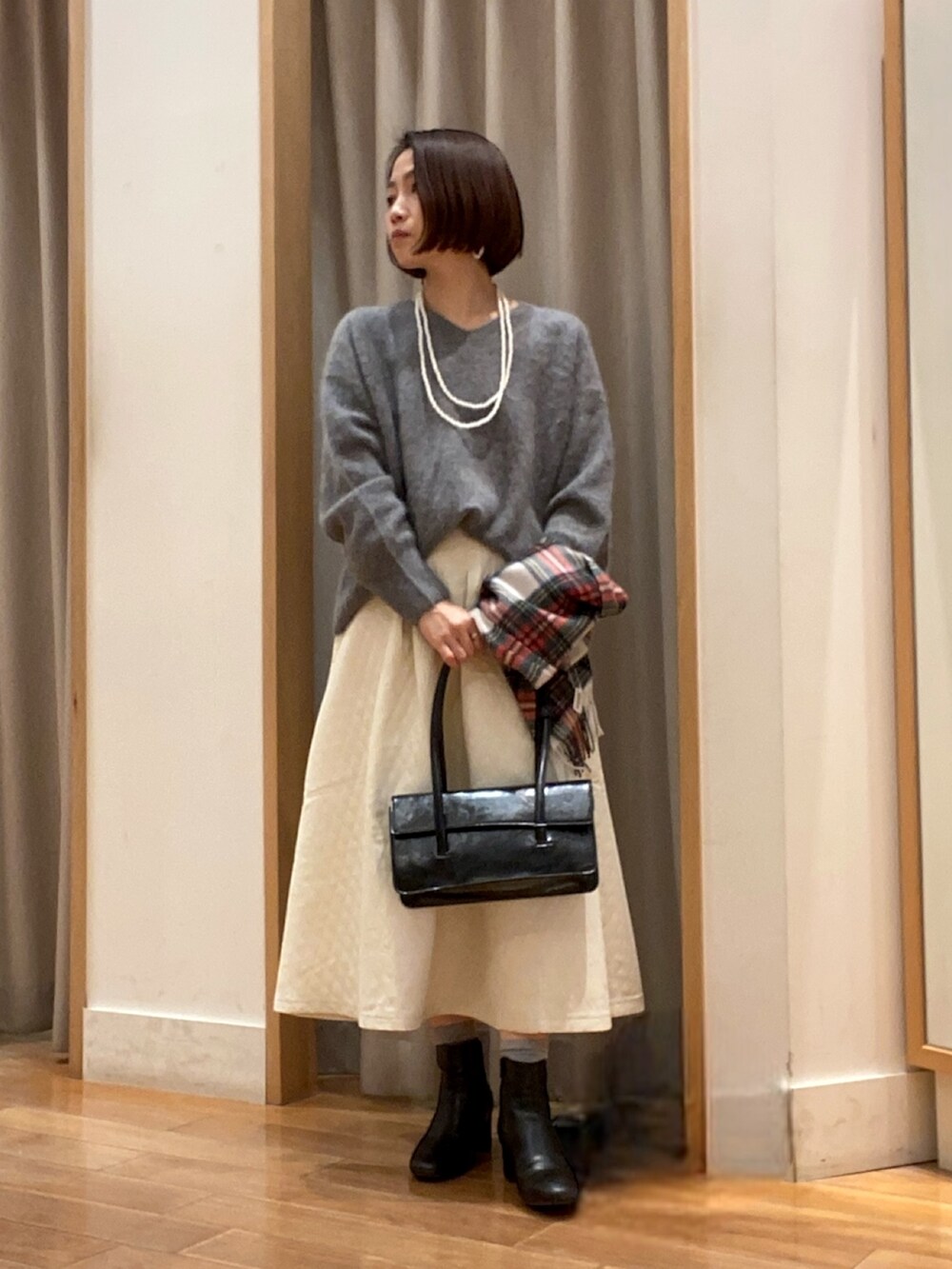 グレー系のニット/セーター、ホワイト系のスカート、ブラック系のハンドバッグを着用したレディースの冬コーディネートの2枚目の写真
