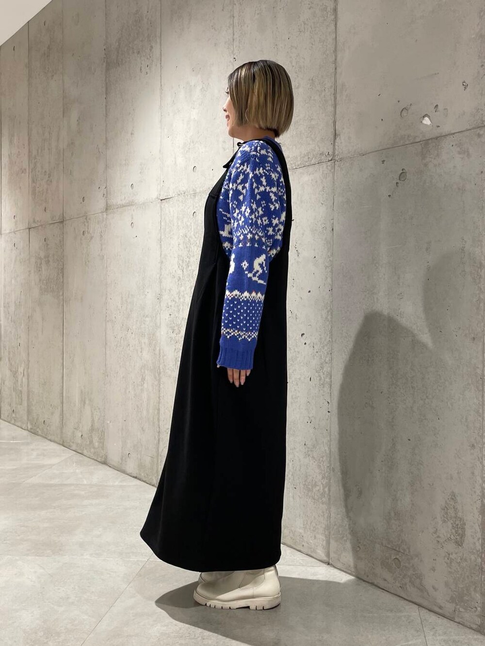 ブラック系のジャンパースカート、ブルー系のニット/セーターを着用したレディースの冬コーディネートの2枚目の写真