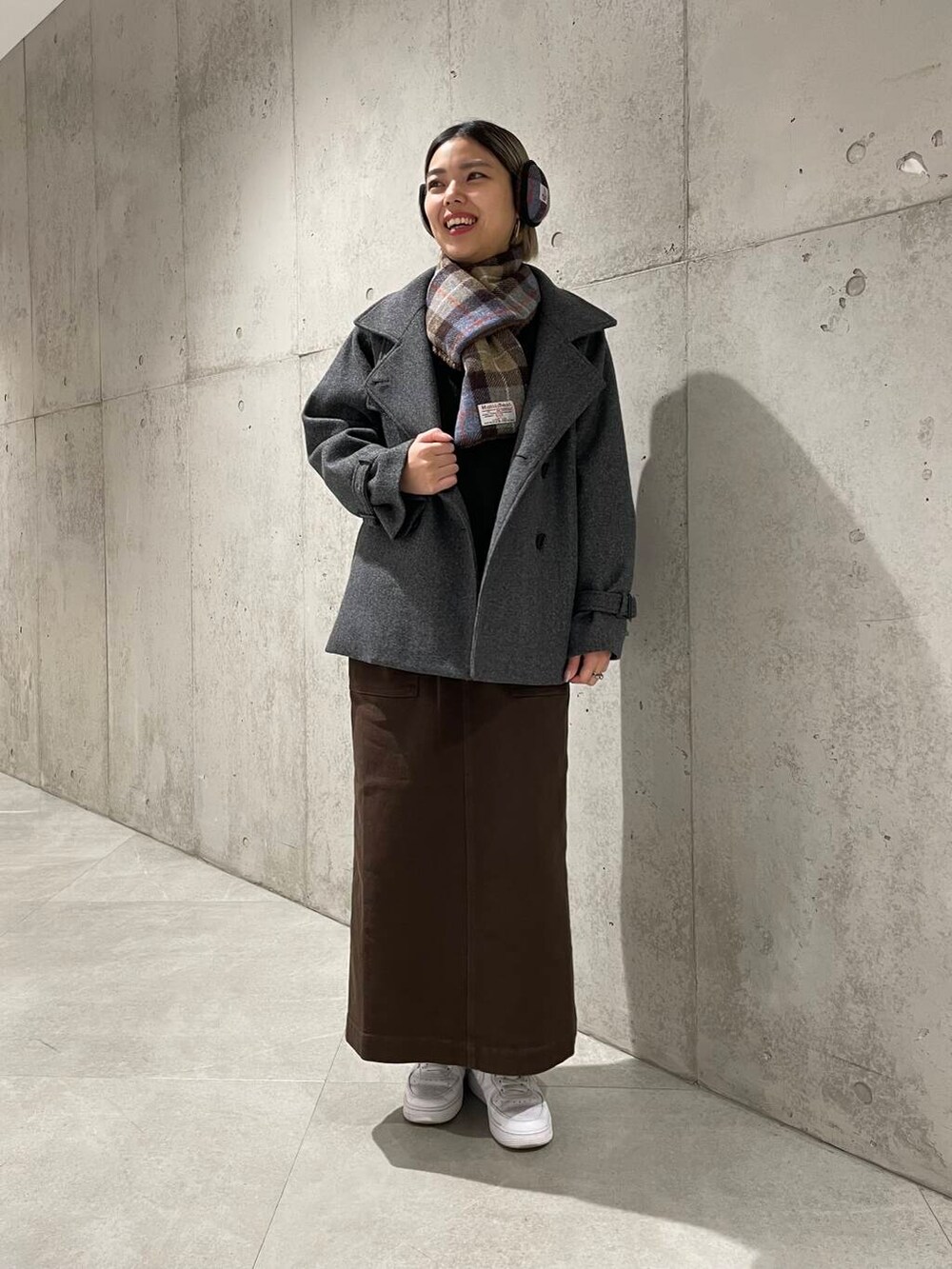 グレー系のトレンチコート、ブラック系のニット/セーター、ブラウン系のスカートを着用したレディースの冬コーディネートの2枚目の写真