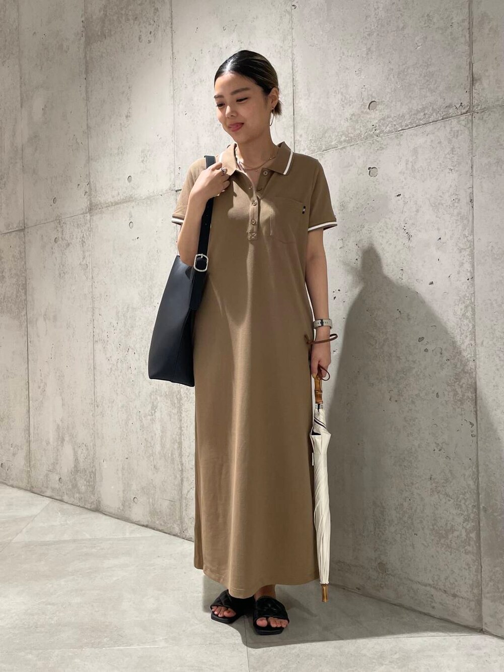 ブラック系のショルダーバッグ、ベージュ系のワンピース、ホワイト系の長傘を着用したレディースの夏コーディネートの2枚目の写真