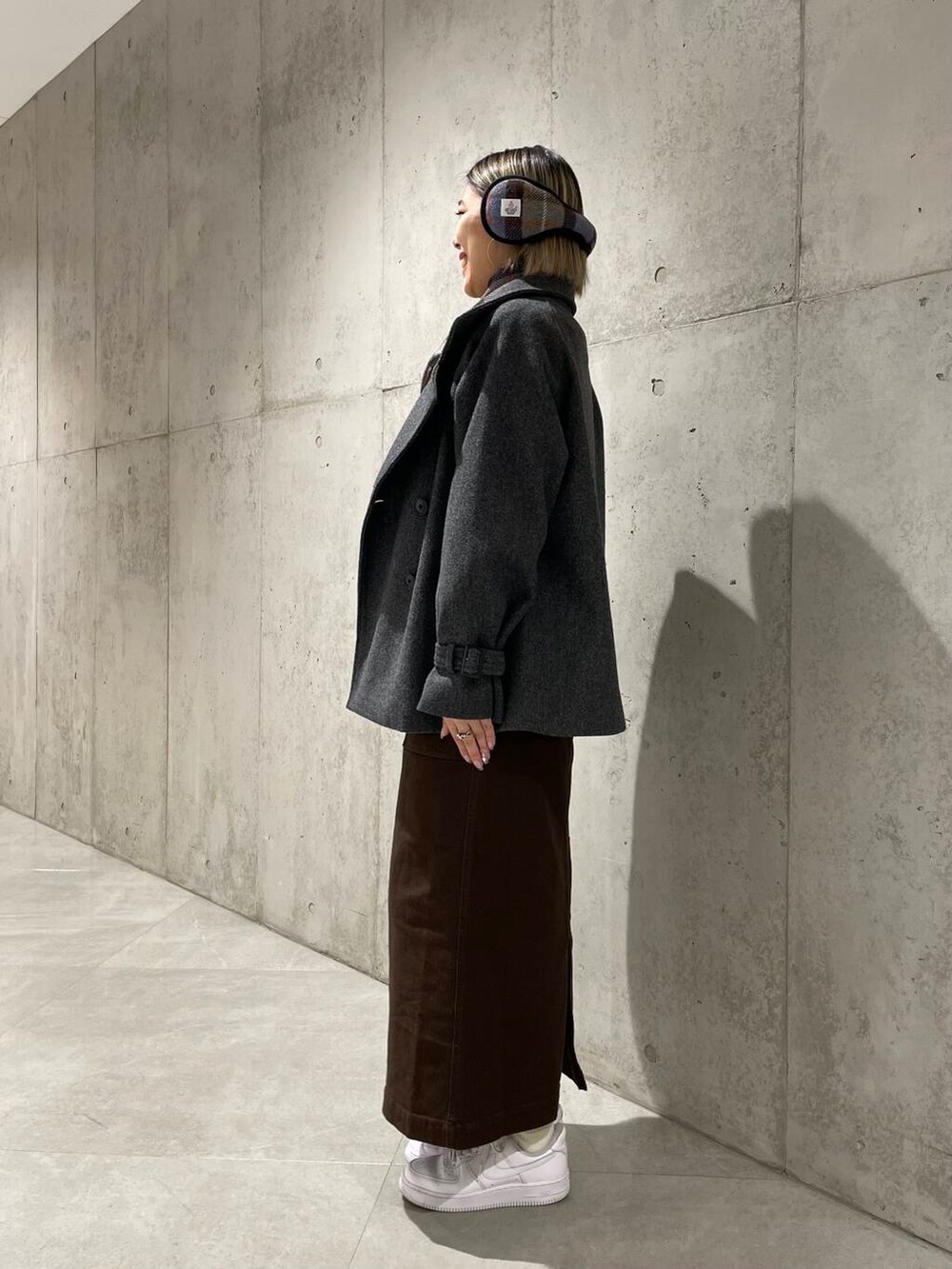 グレー系のトレンチコート、ブラック系のニット/セーター、ブラウン系のスカートを着用したレディースの冬コーディネートの3枚目の写真