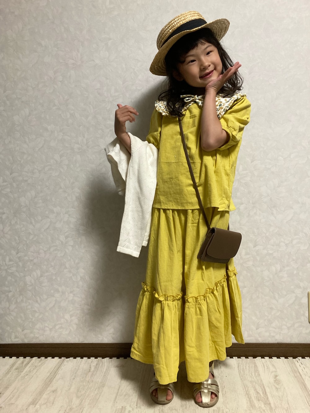 イエロー系のセットアップ、ホワイト系のカーディガン/ボレロ、ブラウン系のショルダーバッグを着用したキッズの春コーディネートの2枚目の写真