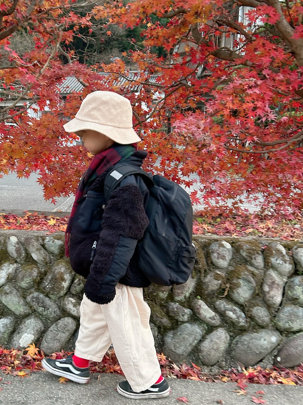 ベージュ系のチノパンツ、ブラック系のバックパック/リュック、ブラック系のスニーカーを着用したキッズの冬コーディネートの2枚目の写真