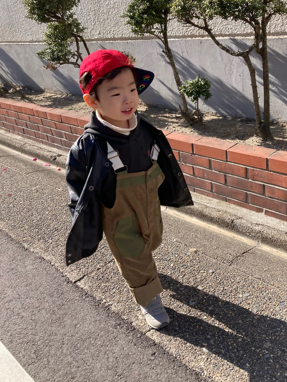ブラック系のパーカー、グリーン系のサロペット/オーバーオール、グレー系のスニーカーを着用したキッズの冬コーディネートの3枚目の写真