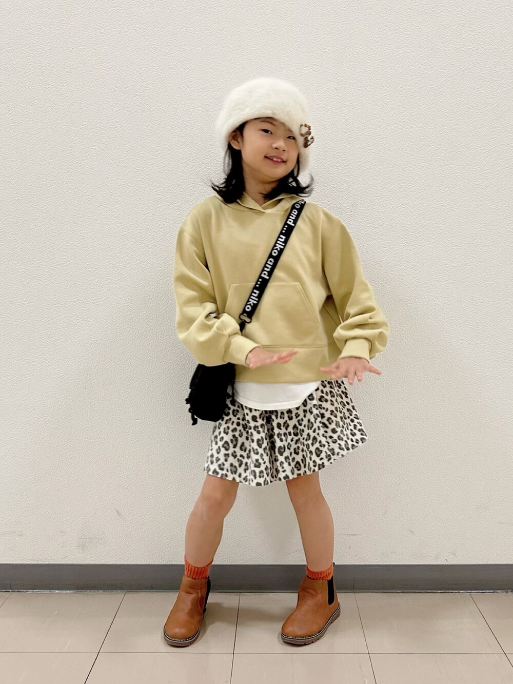 イエロー系のパーカー、ブラック系のショルダーバッグ、ベージュ系のスカートを着用したキッズの冬コーディネートの2枚目の写真