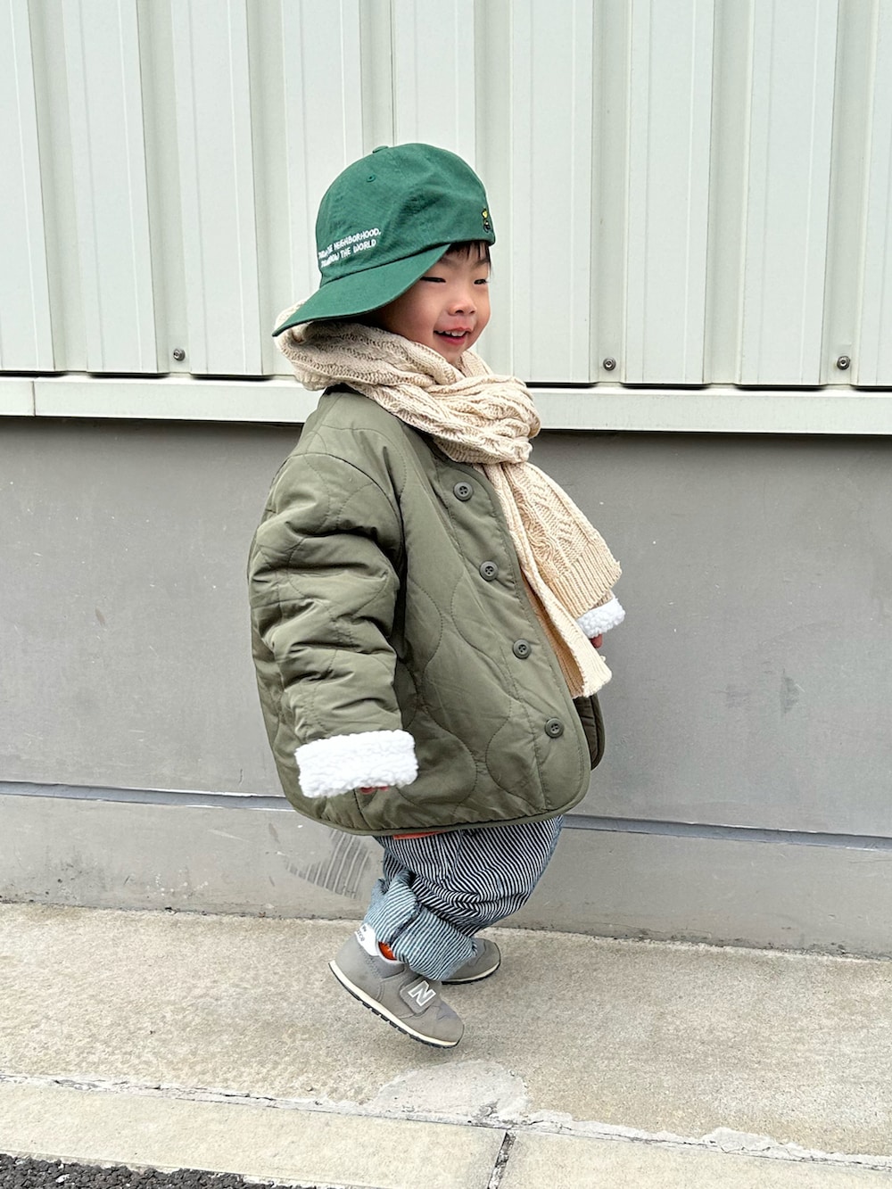 オレンジ系のスウェット、グリーン系のノーカラージャケット、ブルー系のデニムパンツを着用したキッズの冬コーディネートの4枚目の写真