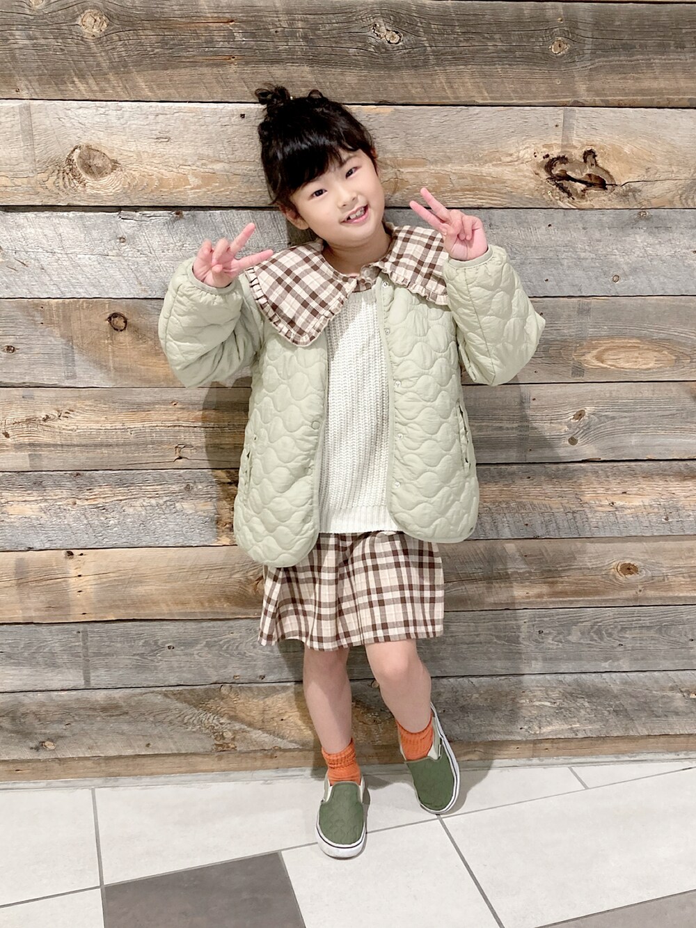 グリーン系のブルゾン、ブラウン系のシャツワンピース、ベージュ系のベストを着用したキッズの冬コーディネートの2枚目の写真