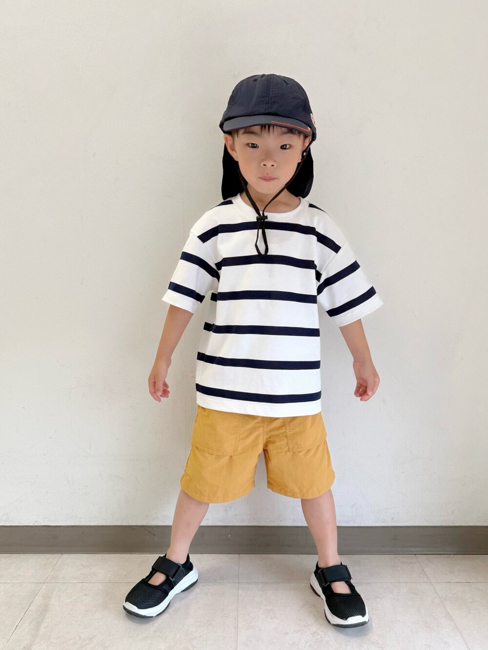 ブラック系のサンダル、ホワイト系のTシャツ/カットソー、ベージュ系のパンツを着用したキッズの夏コーディネートの2枚目の写真