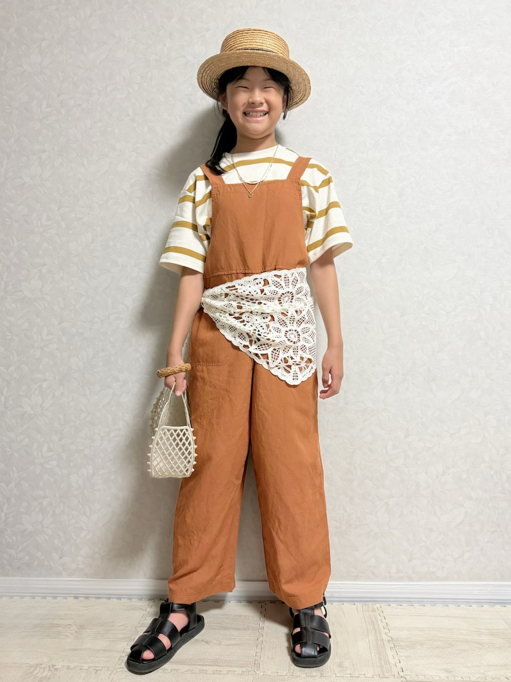 ブラック系のサンダル、ブラウン系のサロペット/オーバーオール、ホワイト系のトートバッグを着用したキッズの夏コーディネートの2枚目の写真