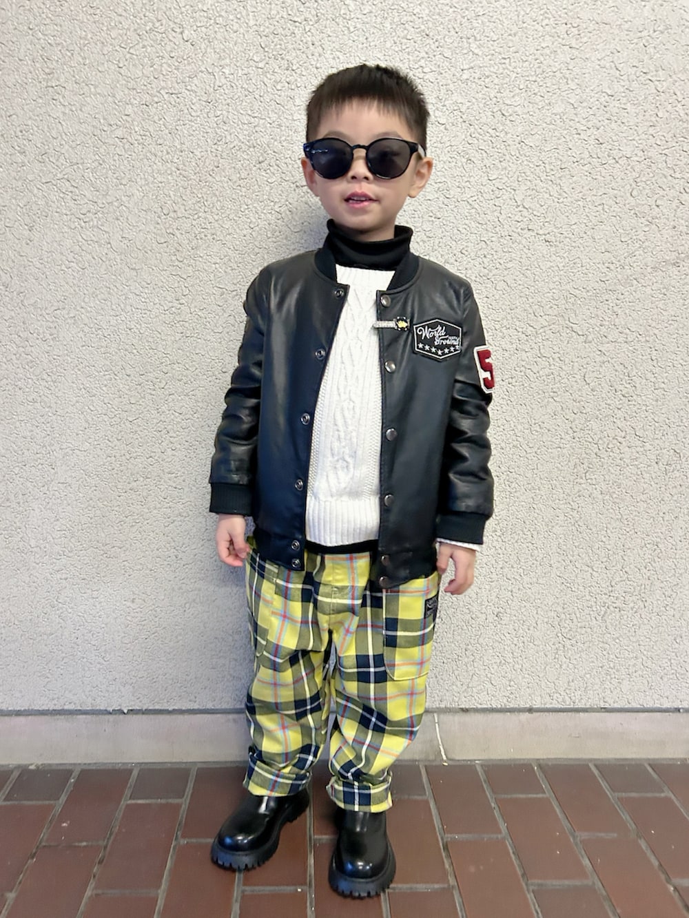 ブラック系のライダースジャケット、ホワイト系のニット/セーター、シルバー系のショルダーバッグを着用したキッズの冬コーディネートの3枚目の写真