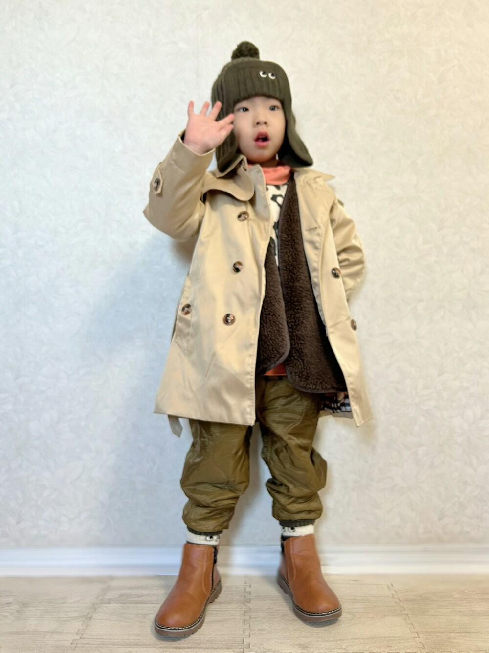 オレンジ系のスウェット、ベージュ系のスウェット、ベージュ系のトレンチコートを着用したキッズの冬コーディネートの2枚目の写真