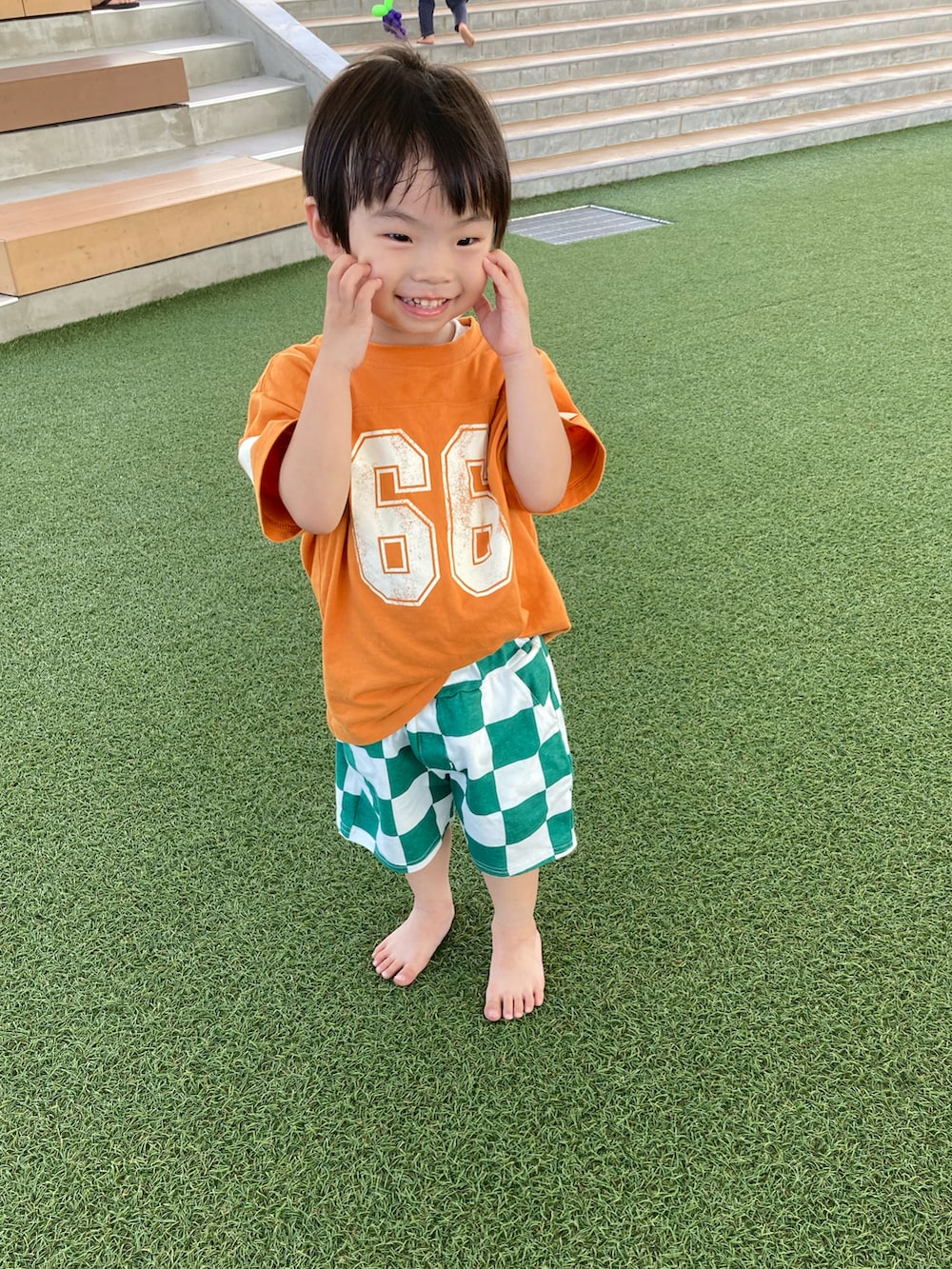 オレンジ系のTシャツ/カットソー、グリーン系のパンツ、ブラック系のサンダルを着用したキッズの夏コーディネートの3枚目の写真