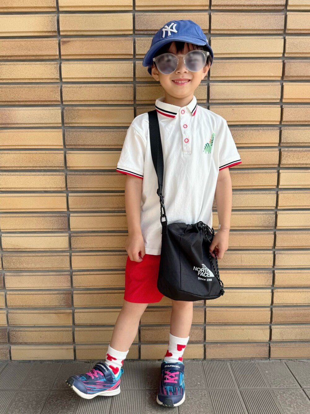 ブラック系のショルダーバッグ、ホワイト系のポロシャツ、ブルー系のスニーカーを着用したキッズの夏コーディネートの2枚目の写真