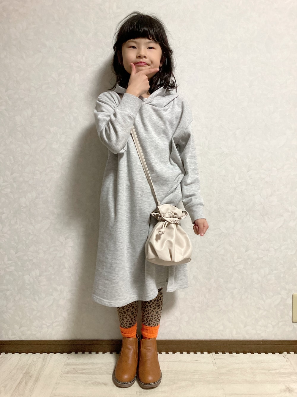 グレー系のワンピース、ホワイト系のショルダーバッグ、ブラウン系のブーツを着用したキッズの冬コーディネートの2枚目の写真