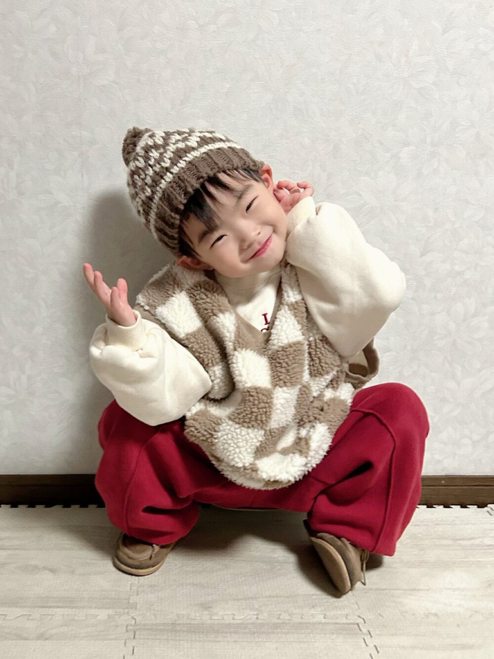 レッド系のセットアップ、ブラウン系のベスト、ベージュ系のブーツを着用したキッズの冬コーディネートの4枚目の写真