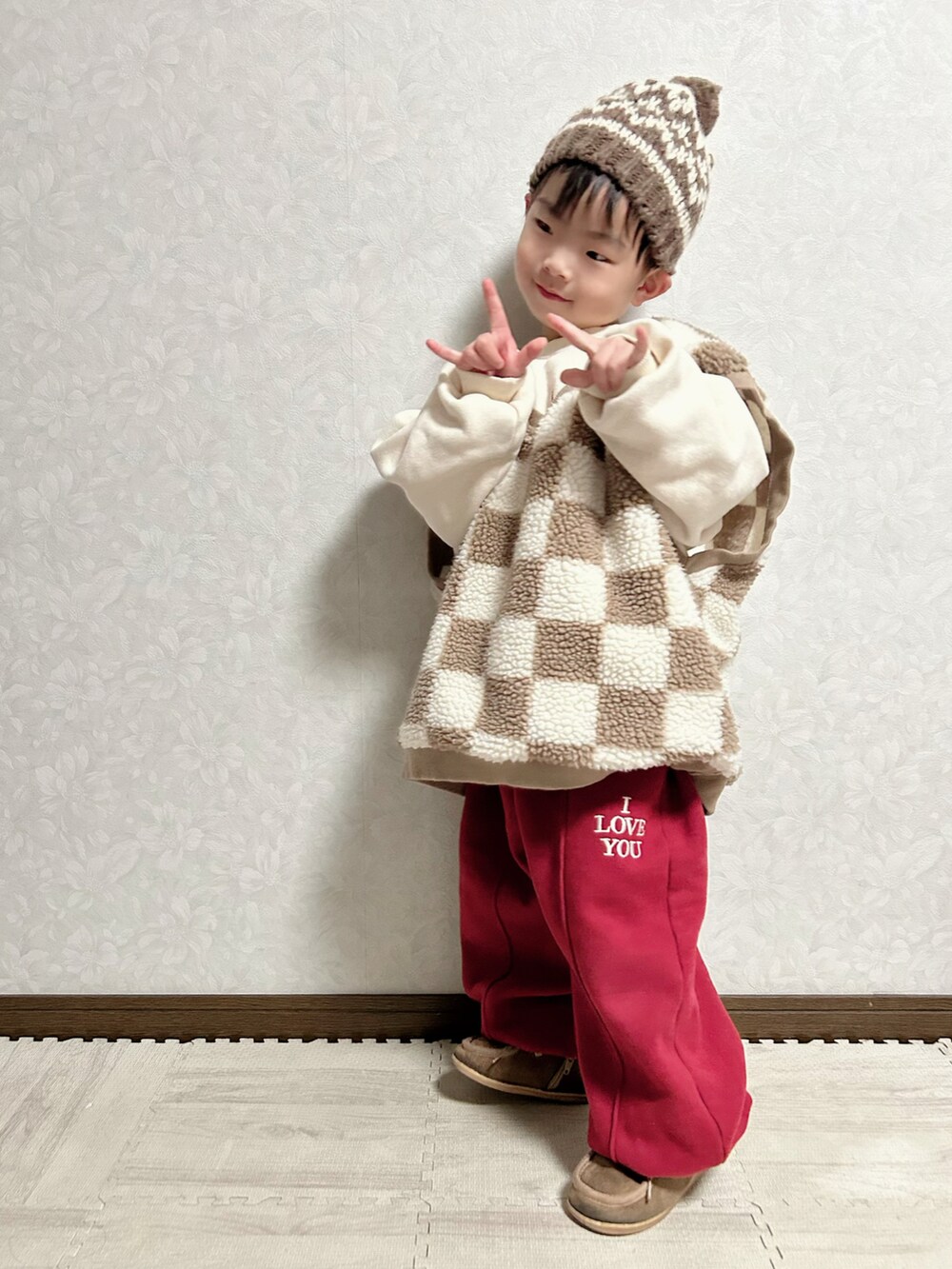 レッド系のセットアップ、ブラウン系のベスト、ベージュ系のブーツを着用したキッズの冬コーディネートの2枚目の写真