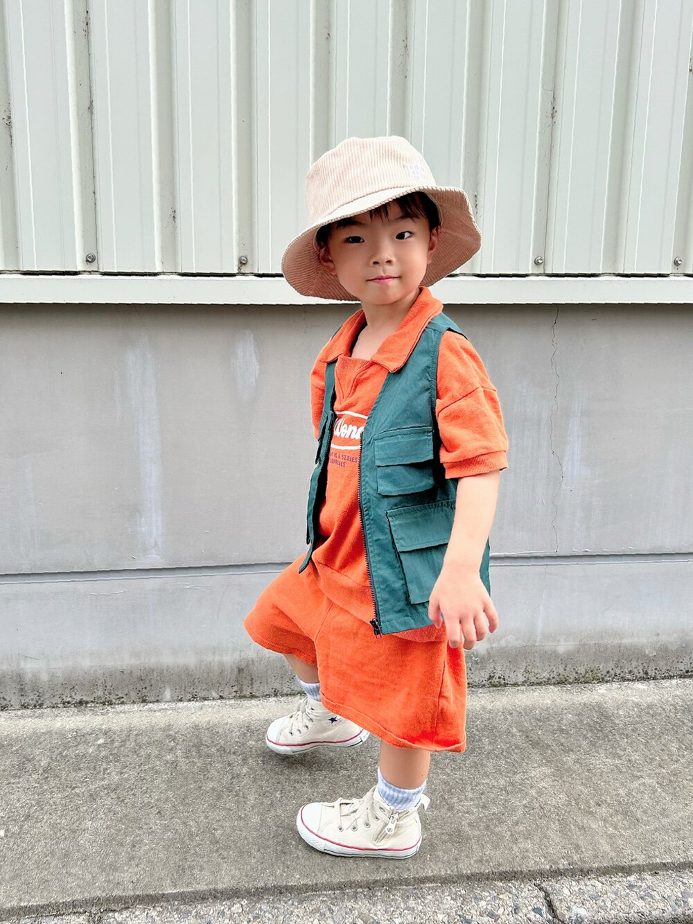 オレンジ系のセットアップ、グリーン系のベスト、ホワイト系のスニーカーを着用したキッズの秋コーディネートの3枚目の写真