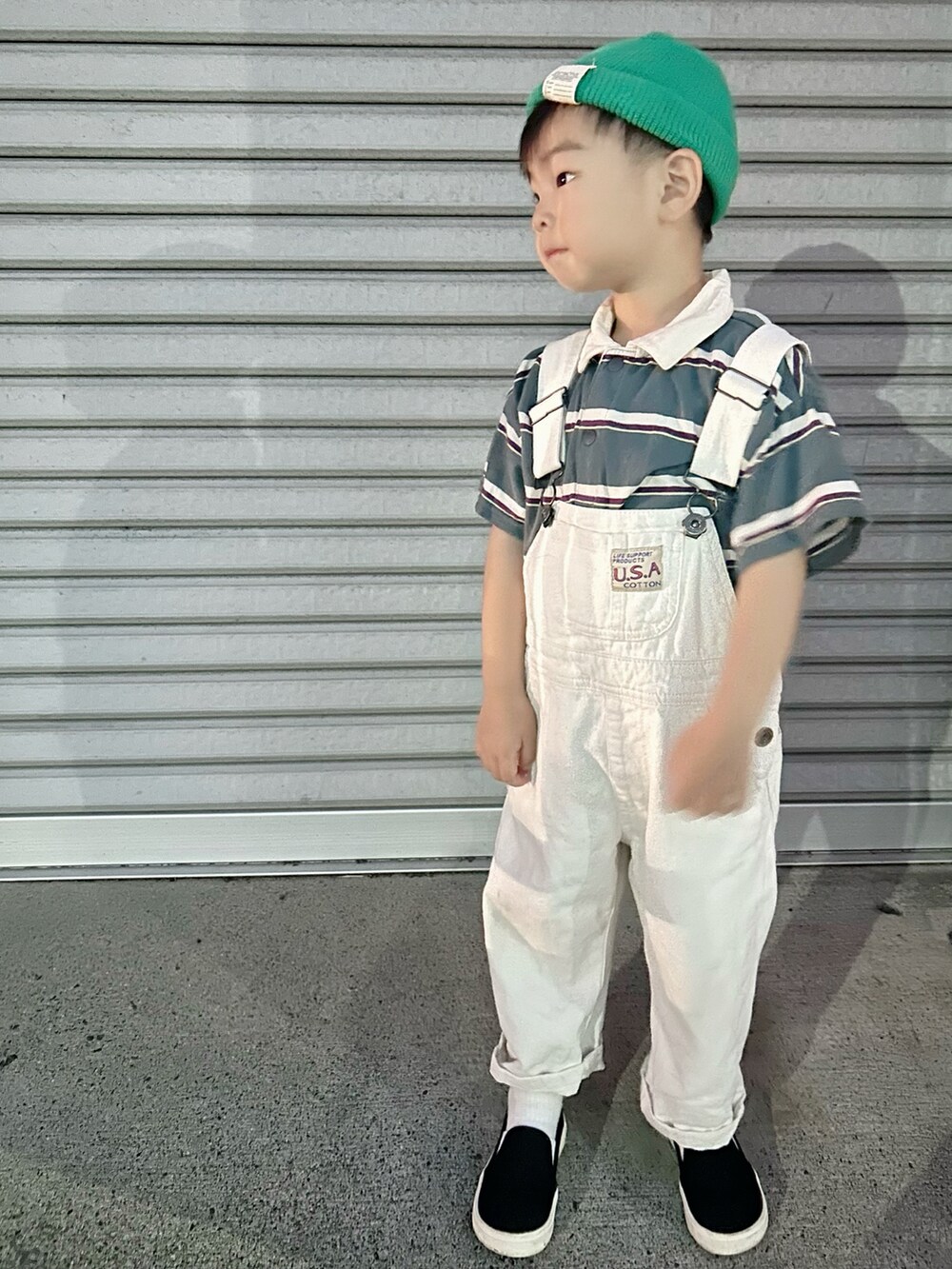 グリーン系のポロシャツ、ホワイト系のサロペット/オーバーオール、ブラック系のスリッポンを着用したキッズの夏コーディネートの3枚目の写真