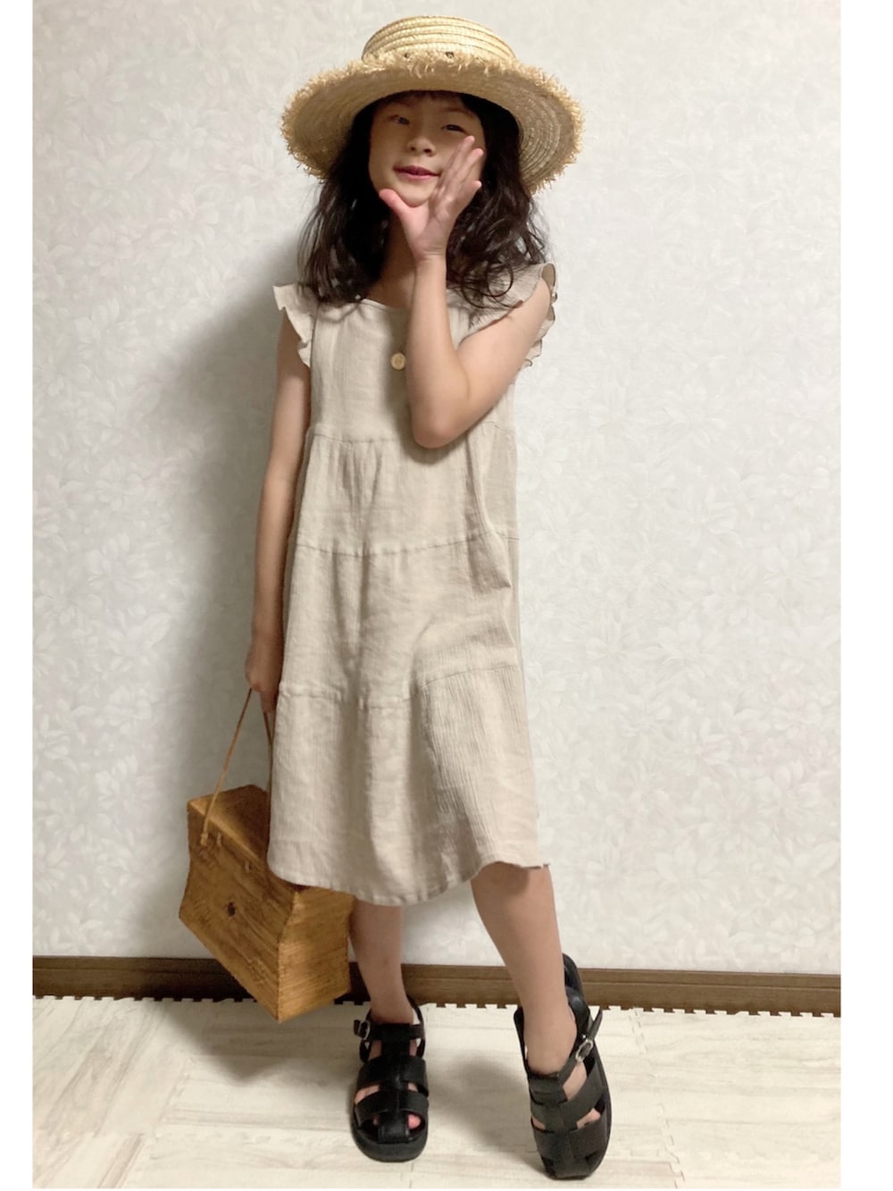 ベージュ系のワンピース、ブラウン系のかごバッグ、ブラック系のサンダルを着用したキッズの夏コーディネートの3枚目の写真