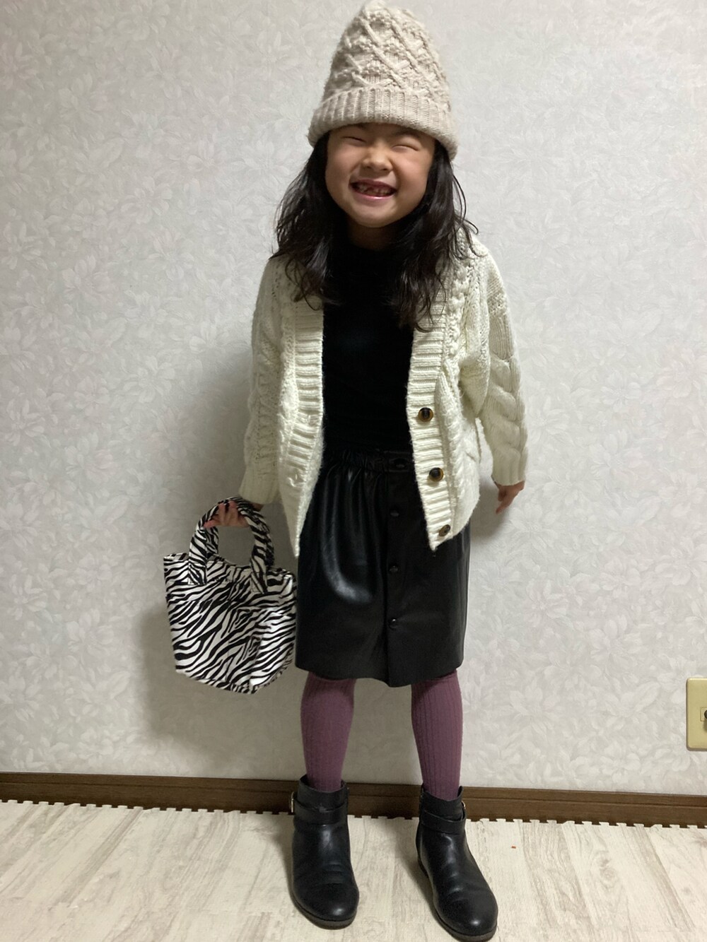 ブラック系のニット/セーター、ホワイト系のカーディガン/ボレロ、ブラック系のスカートを着用したキッズの冬コーディネートの3枚目の写真