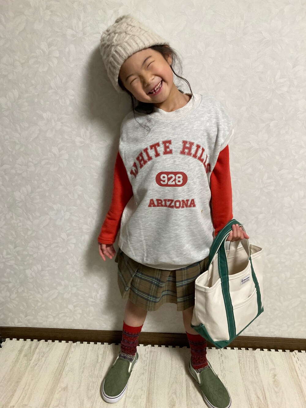 グレー系のベスト、ブラウン系のスカート、グリーン系のトートバッグを着用したキッズの冬コーディネートの2枚目の写真