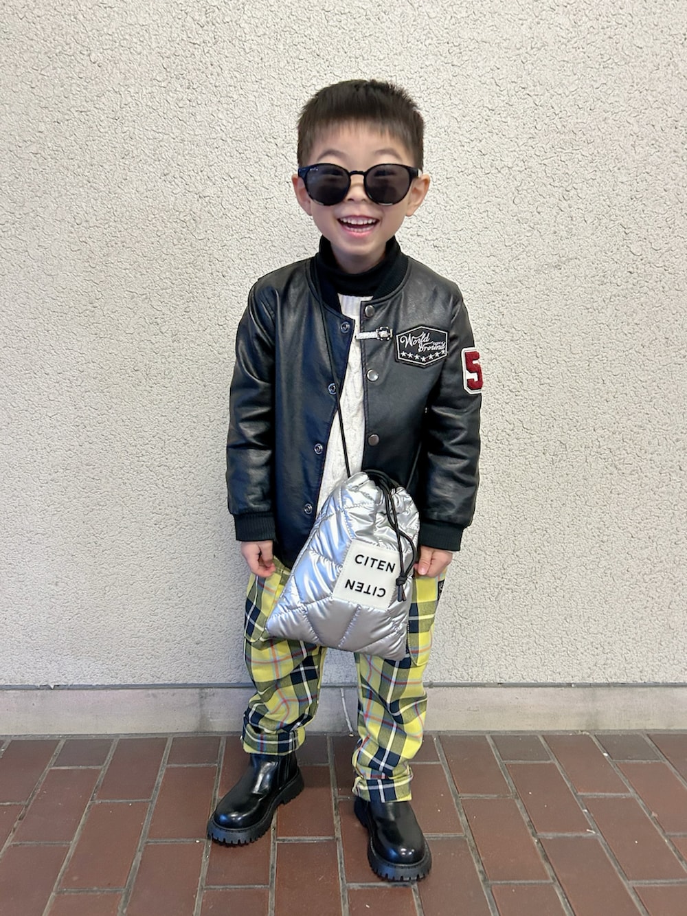 ブラック系のライダースジャケット、ホワイト系のニット/セーター、シルバー系のショルダーバッグを着用したキッズの冬コーディネートの2枚目の写真