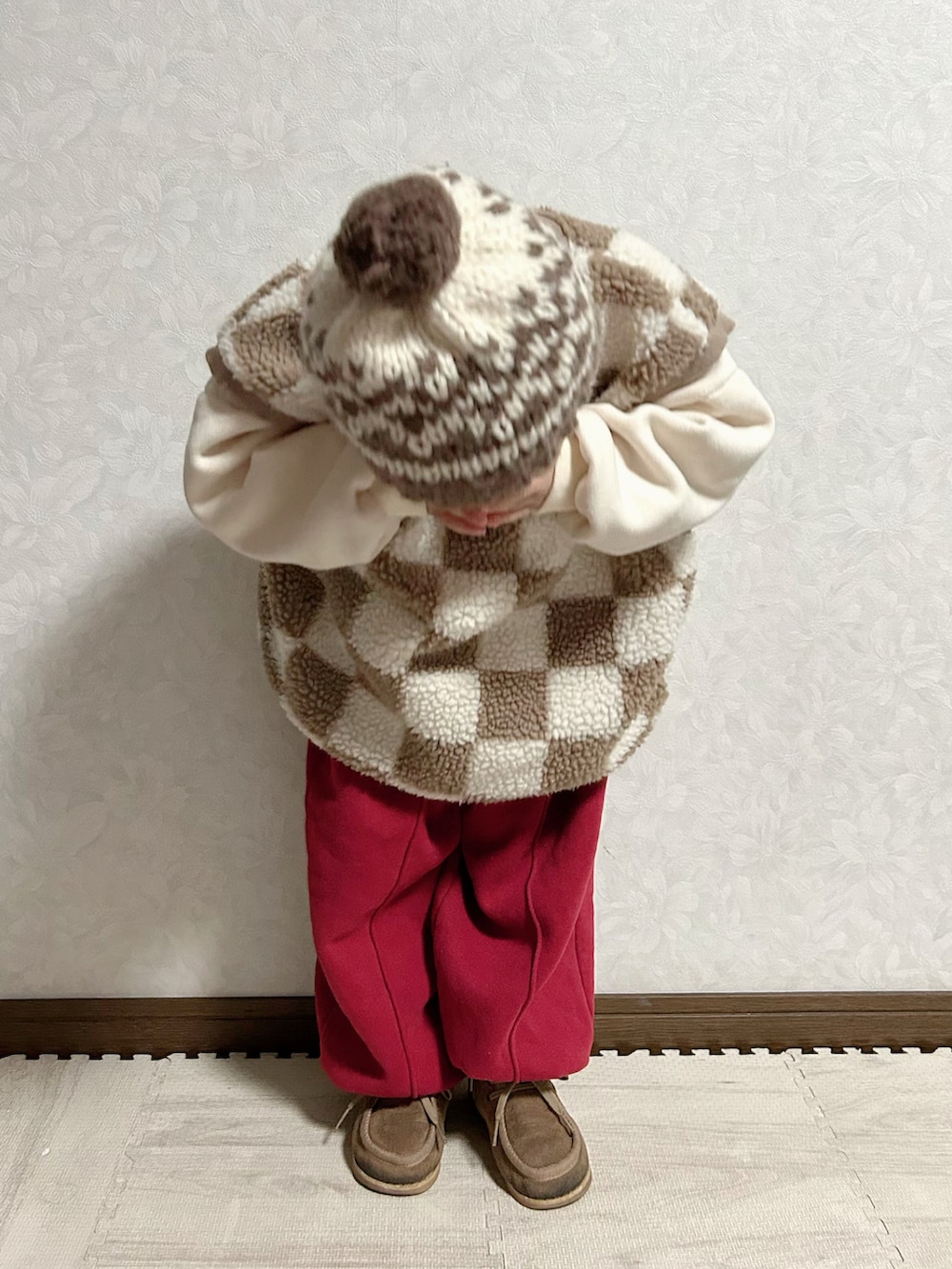 レッド系のセットアップ、ブラウン系のベスト、ベージュ系のブーツを着用したキッズの冬コーディネートの5枚目の写真