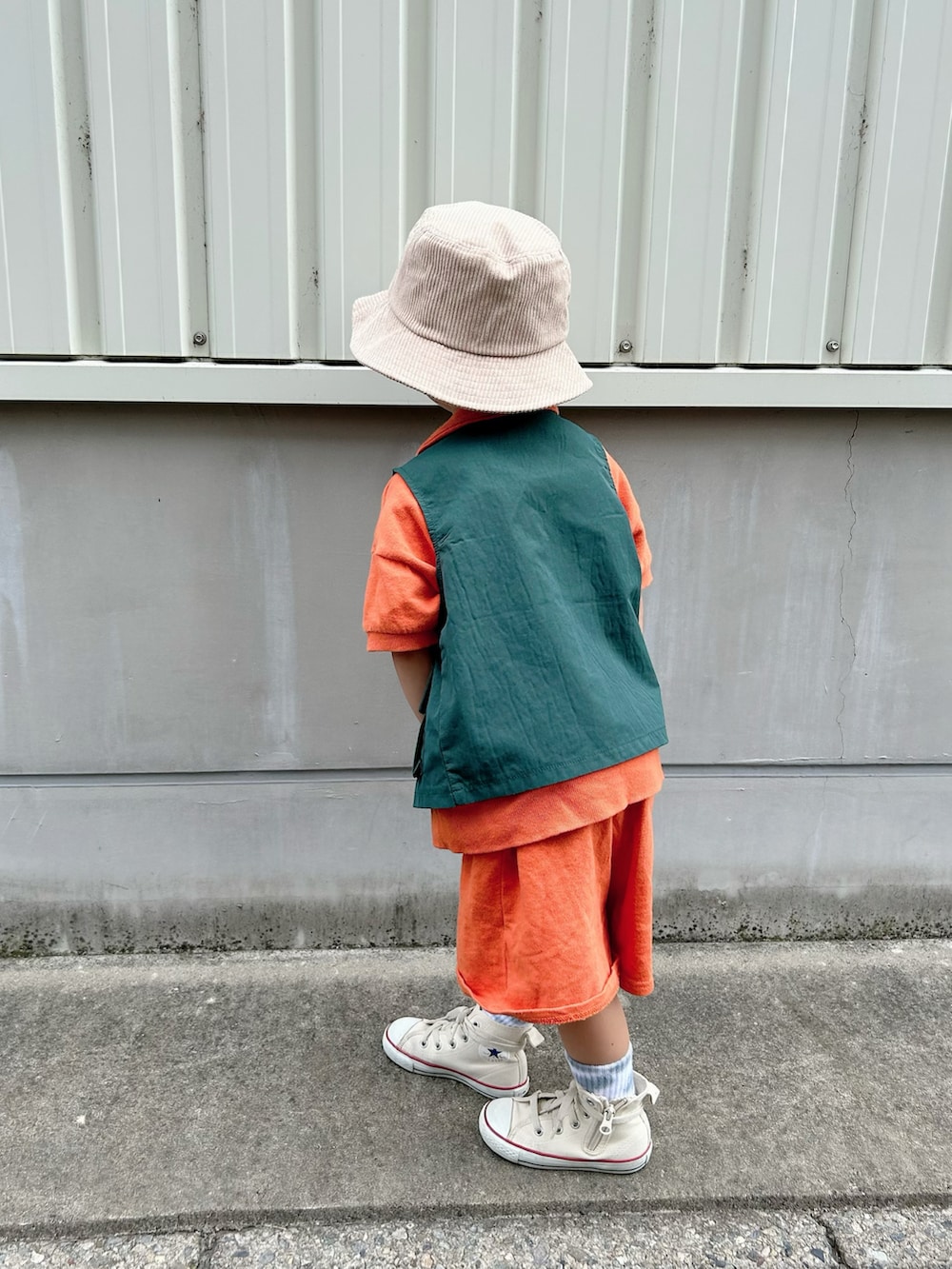 オレンジ系のセットアップ、グリーン系のベスト、ホワイト系のスニーカーを着用したキッズの秋コーディネートの5枚目の写真