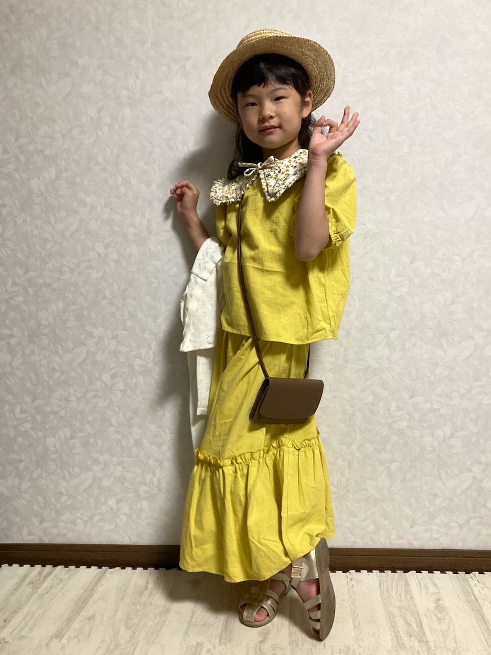イエロー系のセットアップ、ホワイト系のカーディガン/ボレロ、ブラウン系のショルダーバッグを着用したキッズの春コーディネートの3枚目の写真